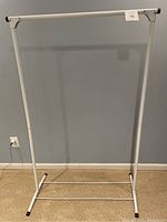 Full view of the white metal collapsible wardrobe rack standing against a wall showing its basic structure with horizontal bar for hanging clothes.