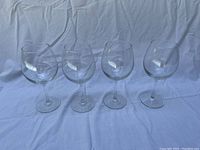 Four identical clear glass wine glasses or water goblets arranged in a row on white fabric showing full items.