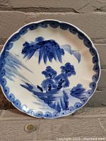 Full view of round scalloped porcelain plate painted with blue mountain landscape, showing overall design and condition.