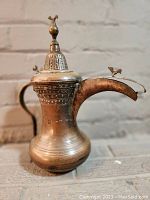 Side view of the solid brass Arabic coffee pot showing intricate etching and bird figurine on the spout tip.