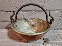 Copper cooking pot from angled front showing cast iron handle and interior condition with oxidation and patina.