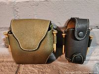 Front view of olive green and black leather golf ball holders showing snap closures and metal tees