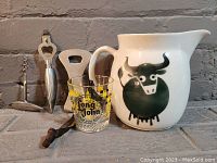 Group photo showing vintage Arabia ceramic jug with black bull design, two cast aluminum vintage bottle openers, vintage corkscrew, and Long John glass.