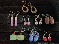 Seven pairs of assorted earrings laid on black background, showing variety of shapes, colors, and materials.