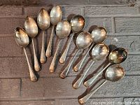 All eleven spoons laid out in a row for full view. Shows size variations and overall condition with tarnish and patina.