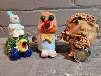 All three ceramic figures shown together: a tortoise with a rabbit on its shell, a clown, and a bearded man bust for scale reference