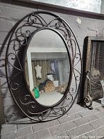Front view of the large oval mirror showing reflective glass and intricate heavy metal scroll frame.