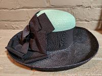 Photo of one Lilliput straw hat showing black brim, light green crown, and voluminous black bow on side.