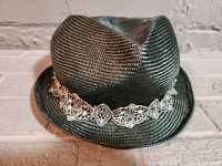 Front angled view of a dark green Lilliput straw hat showing intricate beige lace band detailing fitted around base of crown.