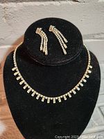 Full view of the necklace and earrings on black display, showing design and condition