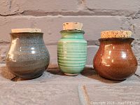 Front and side view of the three miniature ceramic pots showing different colors and shapes, each with an original cork stopper