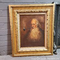 Framed oil painting of an elderly man smoking a pipe shown against a brick wall.