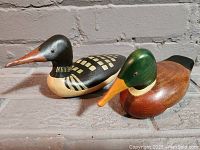 Pair of two hand painted wooden duck decoys on a gray surface against a brick wall background