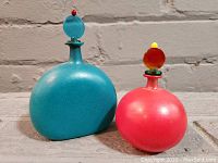 Pair of two handblown Murano perfume bottles, one turquoise blue and one red, positioned together showing size and shape difference.