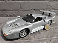 Front quarter angle view of silver Porsche 911 ST diecast model car showing vents, headlights, and detailed wheels, with a coin for scale.