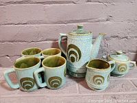 Complete retro tea and coffee set displayed against a brick background showing teapot, sugar bowl, creamer, and four mugs.
