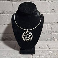 Full view of silver necklace displayed on a black bust against a brick wall background.