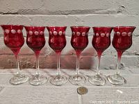 Front view of six cranberry red sherry/port glasses in a row showing white dot etched pattern and clear stems