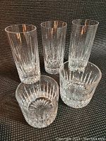 Three tall highball glasses and two short rummers including a larger and smaller rummer in the Stuart Crystal Monaco pattern, displayed on a textured surface.