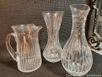 Three clear crystal items including a carafe, water jug, and vase, each with distinct cut glass patterns.