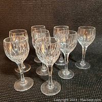 Eight Stuart Crystal sherry glasses arranged standing on a dark surface, showing the vertical cut Monaco pattern and stems.