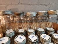 Front view of five antique Crown one-quart mason jars showing clear glass, embossed lettering, and original lids with different metal finishes.