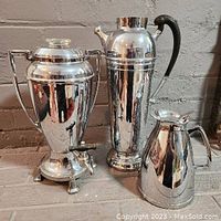 Photo showing three items: a tall coffee urn with spigot, a tall coffee percolator, and a smaller thermos, all with silver-tone finish.