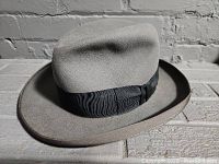 Gray vintage men's felt fedora hat with black ribbon band, showing hat profile and material.