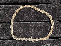 Full view of the silver bracelet showing its intricately linked chain and clasp on black background.