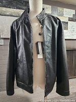 Front view of black vegan leather jacket on mannequin with zipper open showing attached tags, displaying overall style and condition.