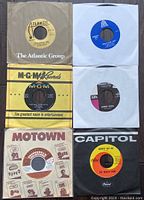 Six 45 RPM vinyl singles from various labels including Atlantic, MGM, Motown, Capitol, and others, showing label designs and sleeve conditions.