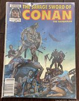 Cover of The Savage Sword of Conan issue 115 with a blue background, showing Conan standing on dead bodies and holding a weapon. Slight wear on edges visible.
