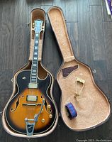 Top-down view of guitar inside open case showing sunburst finish, Bigsby vibrato and accessories