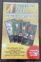 Closed unopened box of Champions of Golf The Masters Collection golf trading cards with gold packaging and images of famous golfers including 1997 Tiger Woods and Mark O'Meara