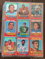 Photo showing 9 vintage 1971 NFL trading cards featuring players like Charlie Sanders (Lions), Larry Brown (Redskins), Jake Scott (Dolphins), John Hadl (Chargers), Mark Moseley (Eagles), Bob Vogel (Colts), MacArthur Lane (Cards), Joe Dawkins (Oilers), Ron Sellers (Patriots).