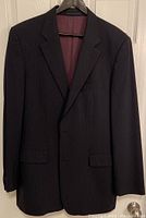 Black pinstripe Hugo Boss suit jacket with burgundy lining hanging on hanger against white door.