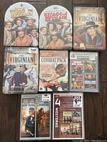 Photo showing 8 unopened Western and War DVD box sets on wooden floor: includes The Virginian, The Wagons West, The Wild Wild West TV series, Combat Pack war movies, and other war and western multi-movie sets.