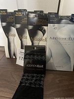 Front view showing four packaged Addition-Elle lace band stay-up hosiery and one package of trouser socks with houndstooth pattern.