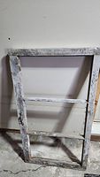 Full view of one antique wooden window frame with three empty pane spaces and chipped paint.