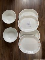 Four oval Corelle serving platters and two round serving bowls on wood floor, showing apricot floral pattern.