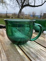 Close-up side view of one teal green Arcoroc oversized mug on a wooden surface outside showing curvature and handle.