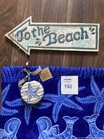 Lot items together showing wooden sign, starfish ornament with tag, and blue scarf with starfish print on wooden floor.