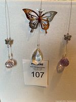 Three butterfly sun catchers displayed against a white background. Center sun catcher has a large silver butterfly and a clear faceted crystal. Left sun catcher has a smaller butterfly and pink faceted crystal. Right sun catcher has a smaller butterfly and light purple faceted crystal. All hanging from thin wire strings.