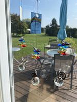 Three Crystal Art sun catchers hanging on a window with rainbow colored crystal segments and clear crystal prisms, showing their reflection and outdoor view.