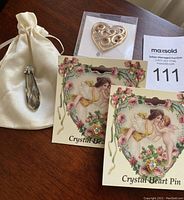 Lot contents display showing two crystal heart pins on decorative vintage-style cards, one heart-shaped crystal sun catcher in plastic packaging, and one large crystal pendant resting on a satin pouch.