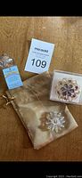 Photo of entire lot on table showing sun catcher in pouch with tag and decorative gem pendant in box