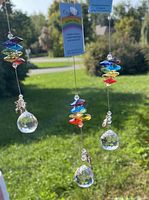 Three brand new Crystal Art sun catchers hanging outdoors against green foliage and blue sky, showing multi-colored crystal beads and clear faceted crystal spheres with pewter charms attached. Said charms are butterfly, unicorn, and elephant.