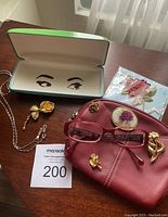 Eyeglass frames, case, chain holders, rose appliqué, brooches and wallet spread on table