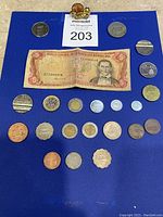 International coins and a 1988 Dominican Republic five pesos paper bill displayed on blue cloth.