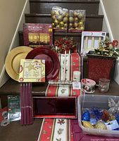 Large lot of Christmas decorations arranged on stairs including electric candoliers, charger plates, boxed ornaments, candles, poinsettia florals and ribbons